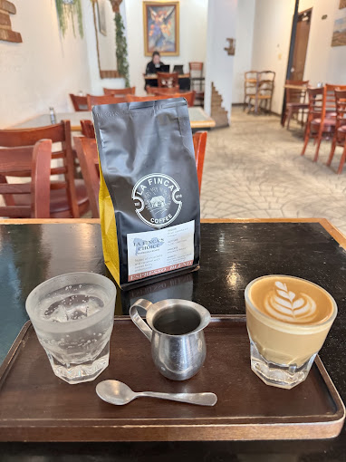 A bag of La Finca coffee beside a cortado and sparkling water on a wood tray